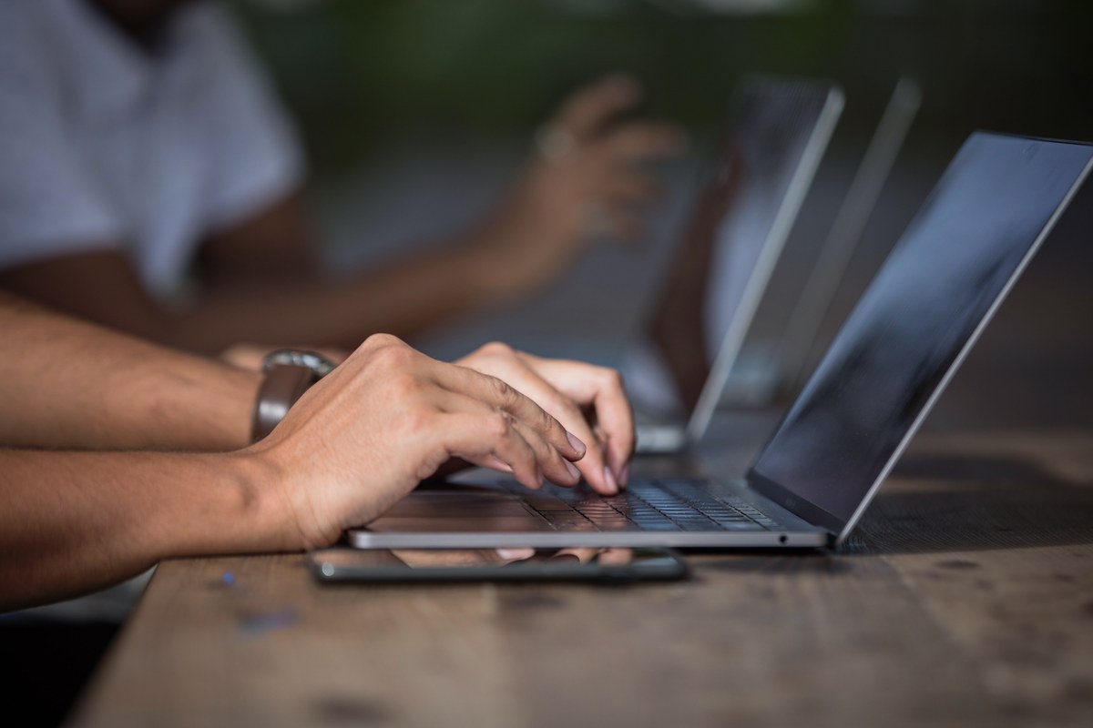 Hands working at two laptops on a shared table.